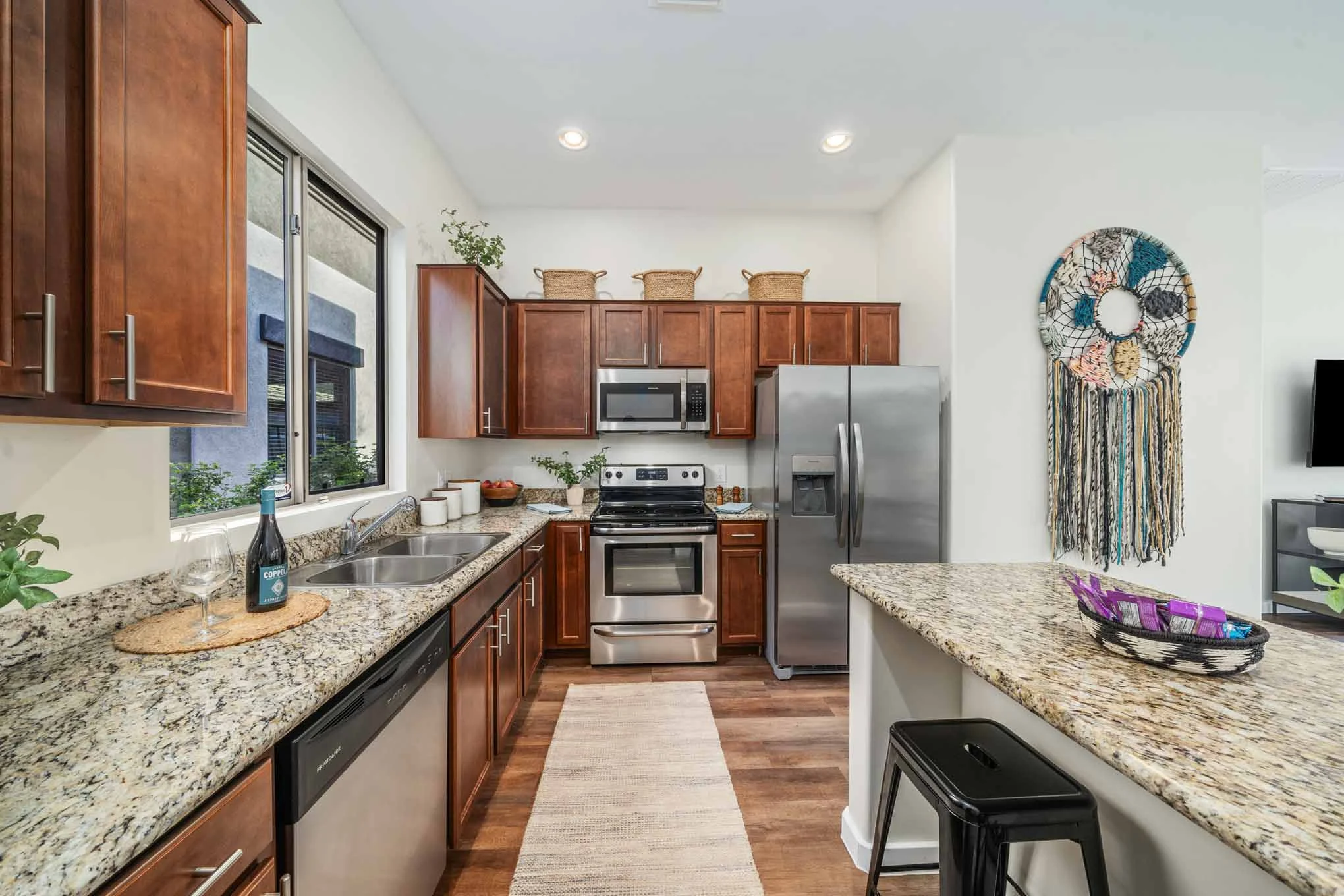 Avilla Marana Modern kitchen with wooden cabinets, stainless steel appliances, granite countertops, and decorative wall art. Bright and airy atmosphere.