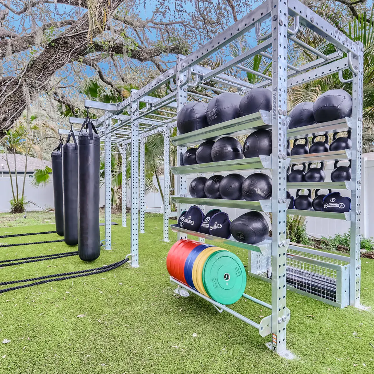 Outside fitness center with weight balls, punching bags, ropes and free weights surrounded by tree's and lawn