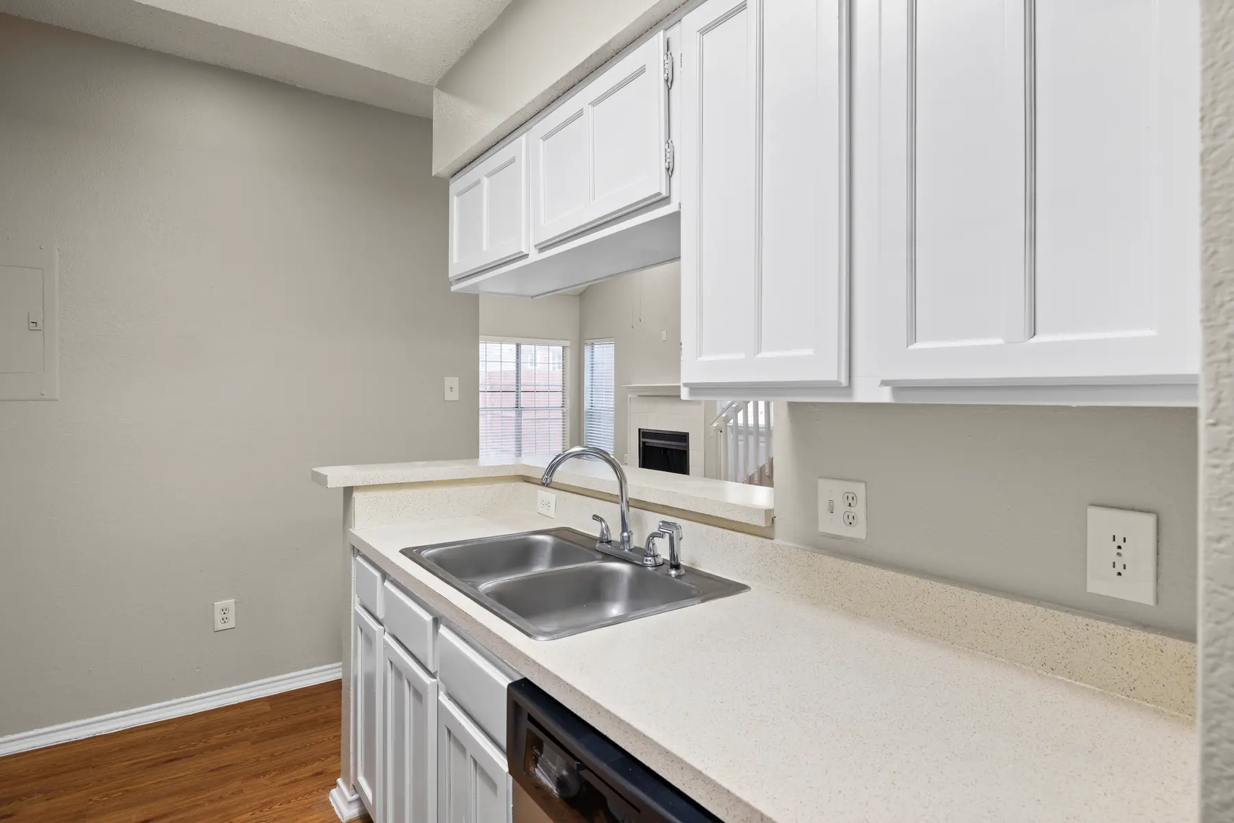 A modern kitchen featuring white cabinetry, a double sink, and a light countertop with wooden flooring.