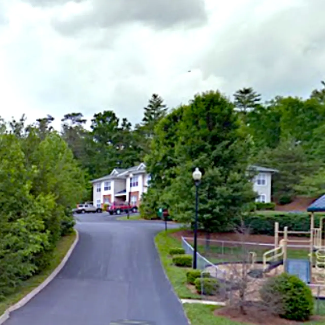 A serene residential area featuring a playground, surrounded by lush greenery and apartment buildings.