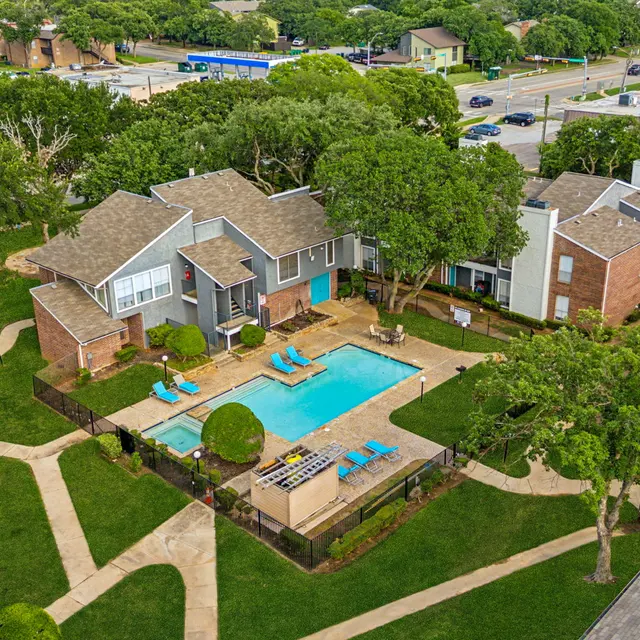 Aerial view of an apartment complex featuring a central swimming pool surrounded by lounge chairs and greenery.