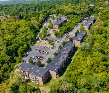 Aerial view of an apartment complex surrounded by lush green trees and parking areas.