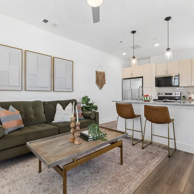 Stylish Modern Living Room A modern living area featuring a green sofa, wooden coffee table, pendant lights, and an open kitchen in the background.