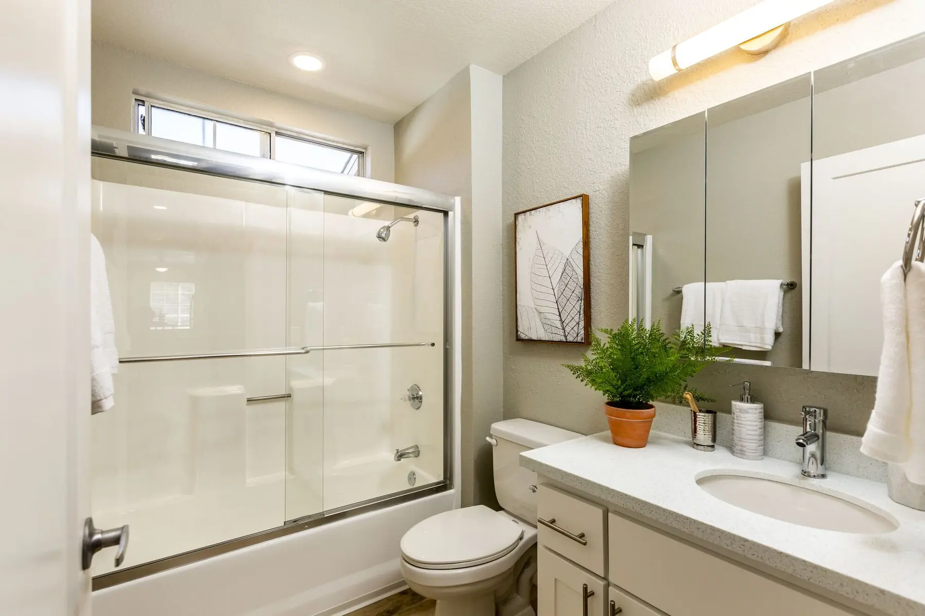 A modern bathroom featuring a glass shower enclosure, a sink with a modern faucet, mirrors, and a decorative plant.