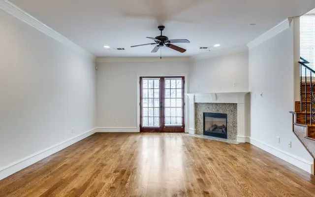 Spacious Living Room with Fireplace A spacious living room featuring wooden flooring, a ceiling fan, and a stone fireplace. There are French doors leading to an outdoor area and a staircase partially visible in the corner.