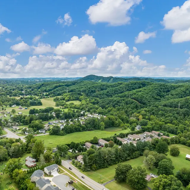 Aerial view of a rural area surrounded by lush green hills and a clear blue sky with fluffy clouds.