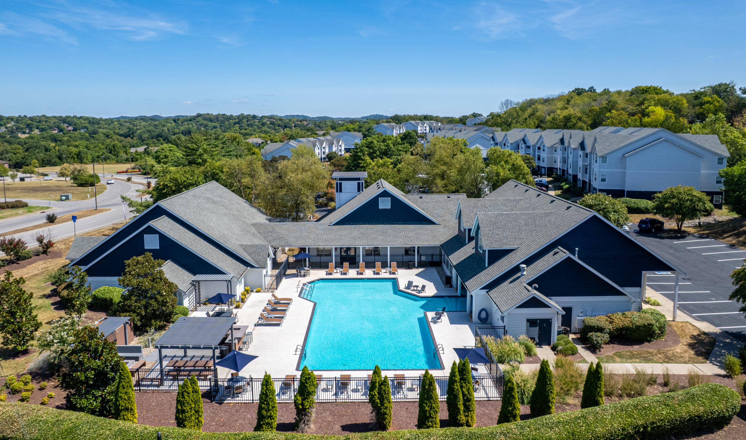 Aerial view of a modern apartment complex featuring a swimming pool surrounded by landscaped gardens and seating areas.