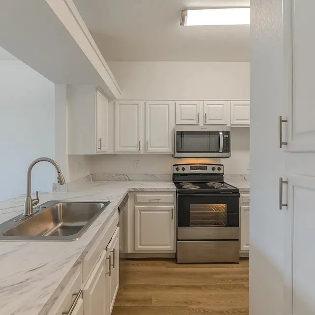 A modern kitchen featuring white cabinets, stainless steel appliances, and marble countertops.