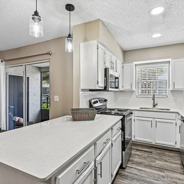 Stylish Modern Kitchen A modern kitchen featuring white cabinetry, stainless steel appliances, and a spacious island with a bowl. The kitchen has a contemporary feel with pendant lighting, a window above the sink, and an open layout leading to an outdoor area.