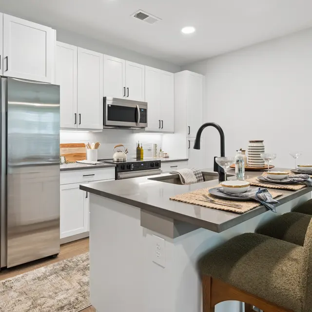 Sleek Modern Kitchen A modern kitchen featuring stainless steel appliances, white cabinets, and a stylish breakfast bar with stools. The countertop is set with dishes and decor, enhancing the inviting atmosphere.