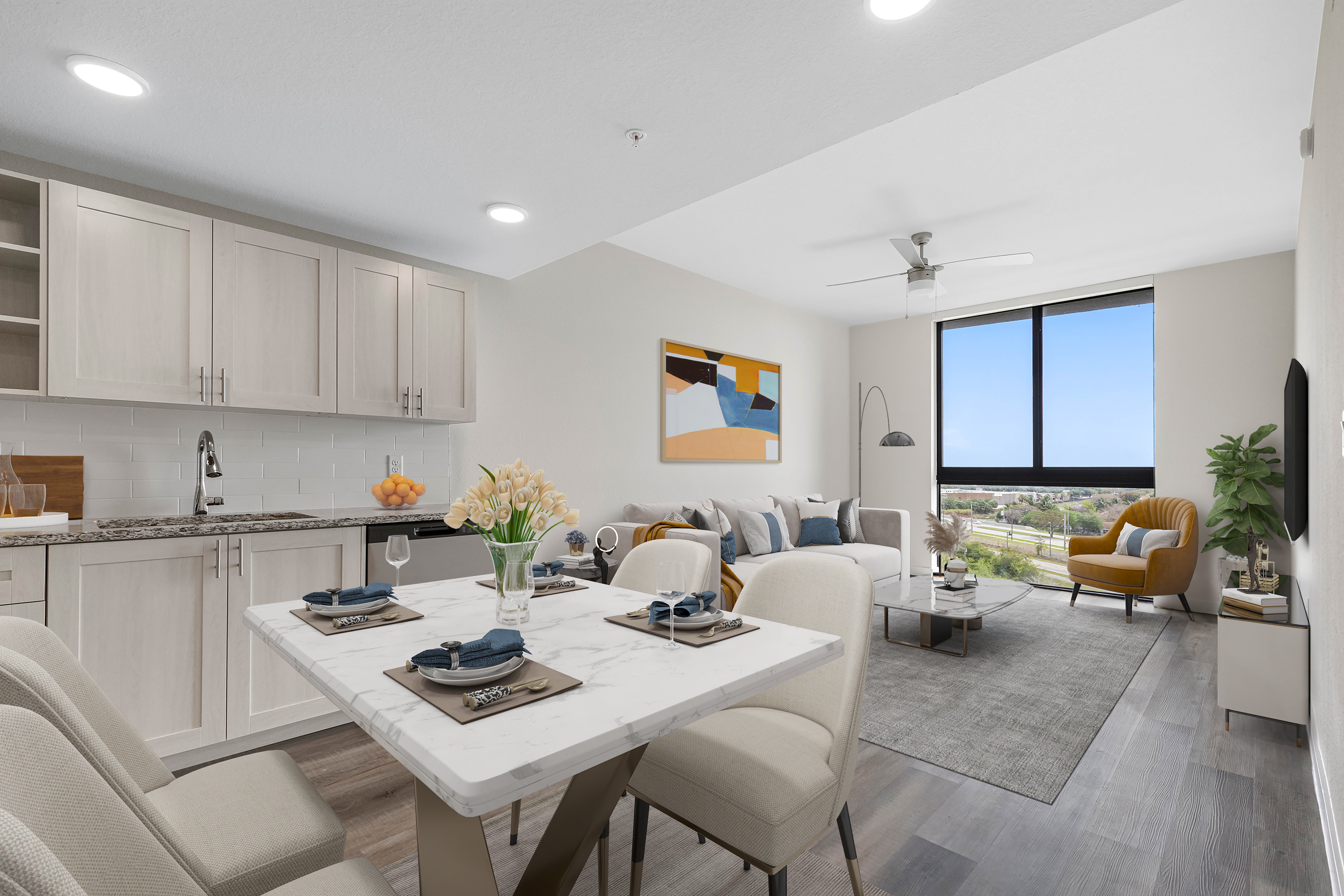 Modern Apartment Living Space A modern apartment interior featuring a kitchen and living area, with a dining table set for two and a cozy couch with decorative pillows. A large window offers a view of the outdoors.