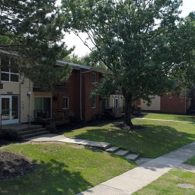 Aerial view of a residential apartment complex with two-story buildings surrounded by trees and grass along a sidewalk.