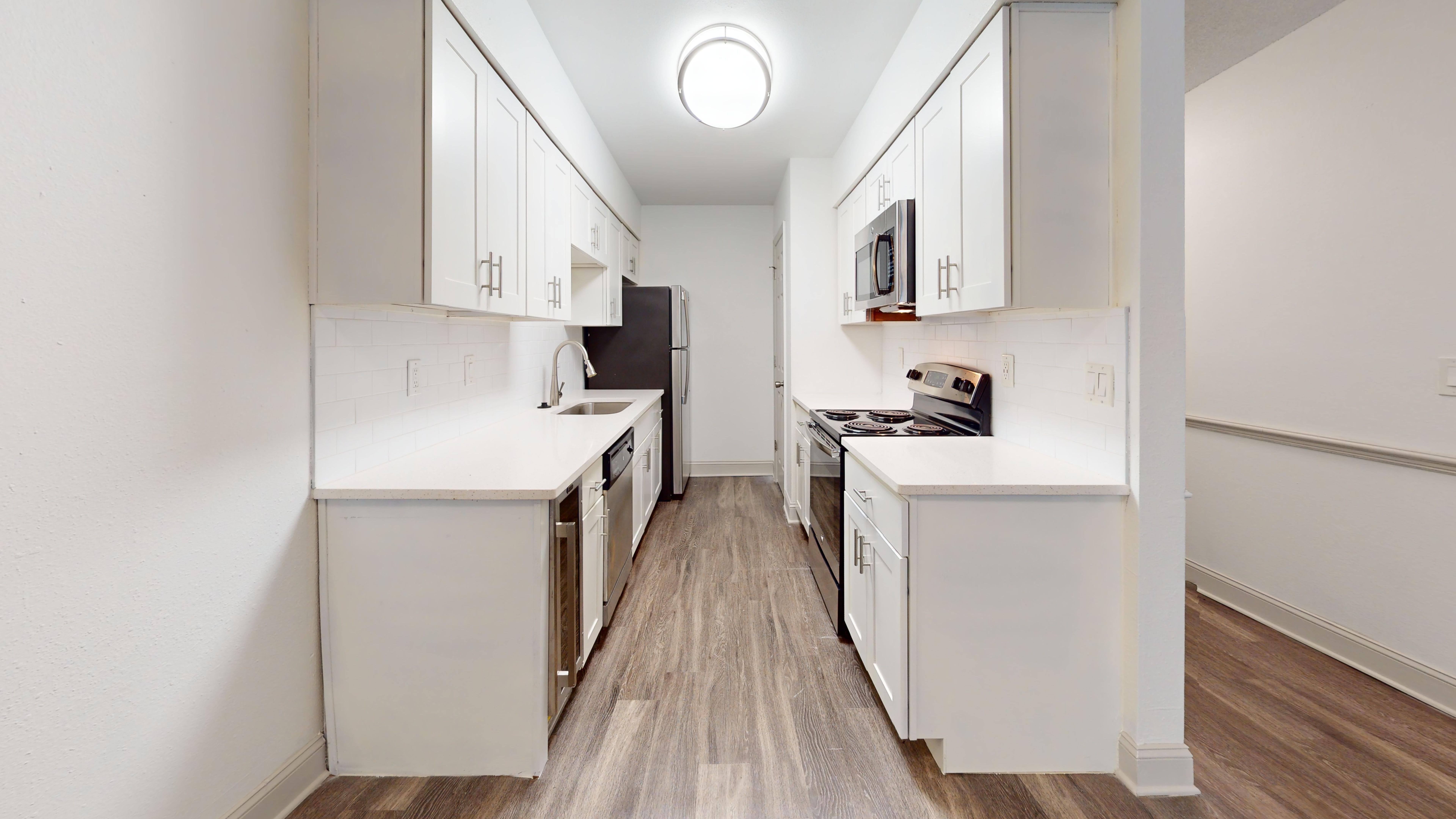 A modern kitchen featuring an L-shaped layout with white cabinets, stainless steel appliances, and a clean, bright appearance.