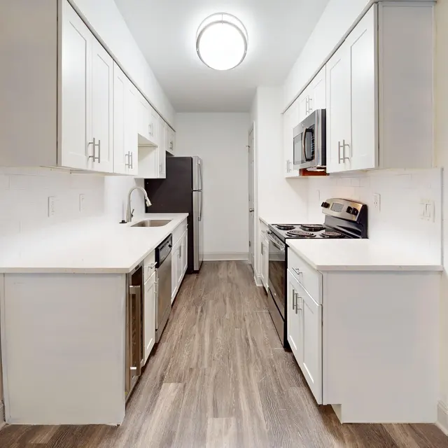 A modern kitchen featuring an L-shaped layout with white cabinets, stainless steel appliances, and a clean, bright appearance.