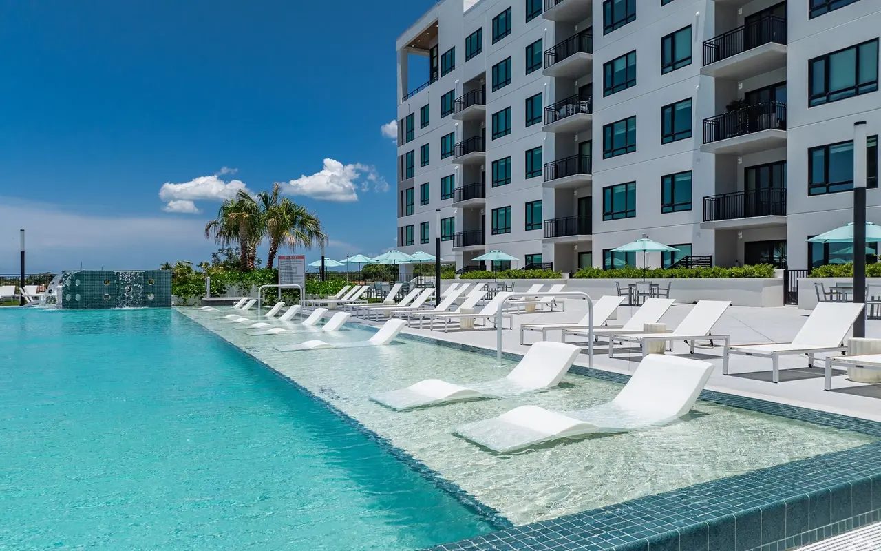 A modern pool with lounge chairs and an apartment building in the background under a clear blue sky.
