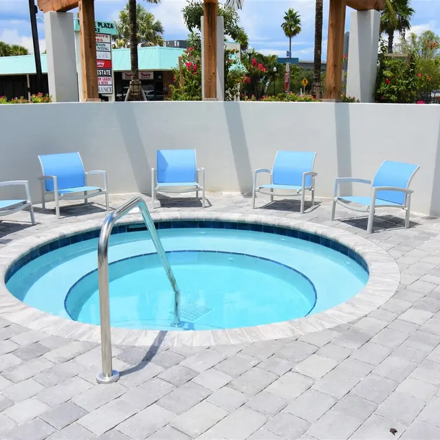 Hot Tub Relaxation Area A hot tub surrounded by light blue chairs on a stone-paved surface, with a white wall and palm trees in the background.