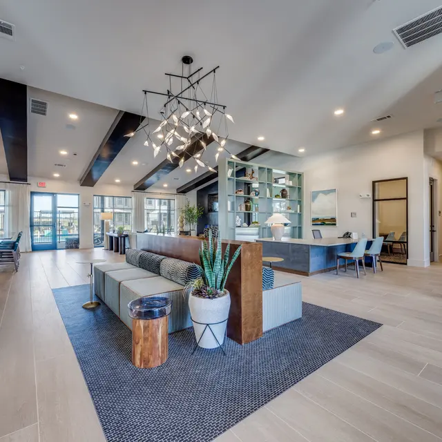 A modern lobby area featuring stylish furniture, a large central seating arrangement with plants, and large windows allowing natural light to fill the space.