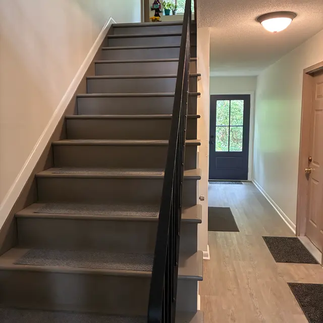 A view of a staircase leading to an upper level, with a landing area visible at the top. The walls are painted light colors with hardwood flooring visible in the hallway.