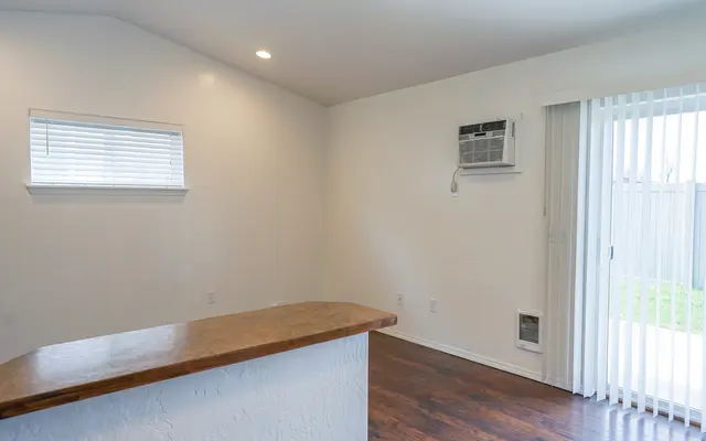 Interior Room Design An interior room with a wooden countertop, a window, and sliding glass doors leading outside. The room features white walls and dark wooden flooring, with an air conditioning unit on the wall.