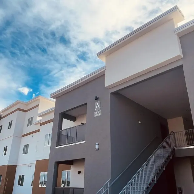 Exterior view of a modern apartment building featuring multiple floors, balconies, and a cloudy sky in the background.