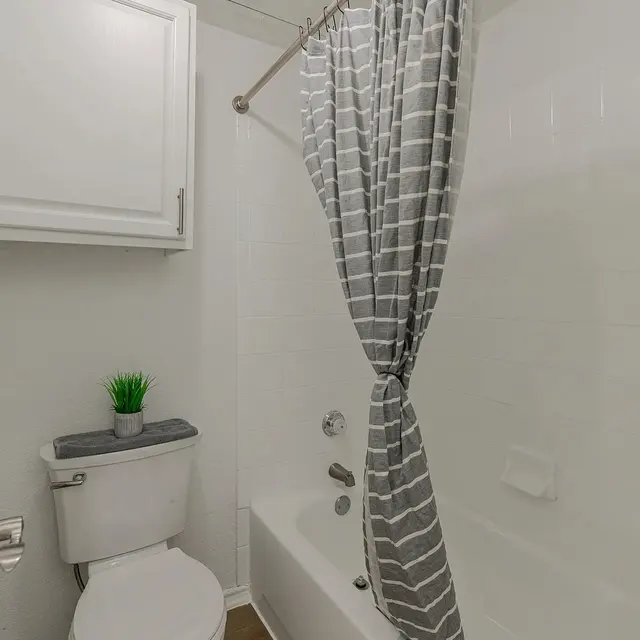 A small bathroom featuring a bathtub, toilet, and gray striped shower curtain.