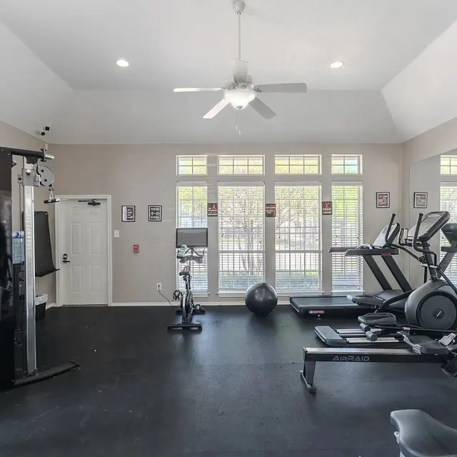 A modern gym interior featuring various fitness equipment including treadmills, a stationary bike, strength training machines, and a large window allowing natural light to stream in.