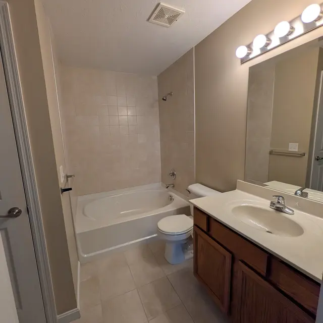 A clean and simple bathroom featuring a bathtub, toilet, and sink with a wooden vanity.