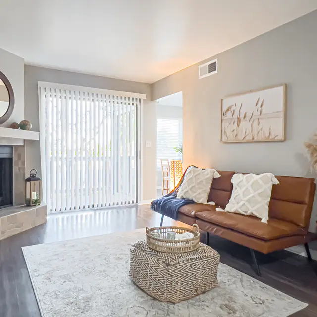 Modern living room with a brown sofa, decorative pillows, a fireplace, window blinds, and a stylish coffee table on a rug.