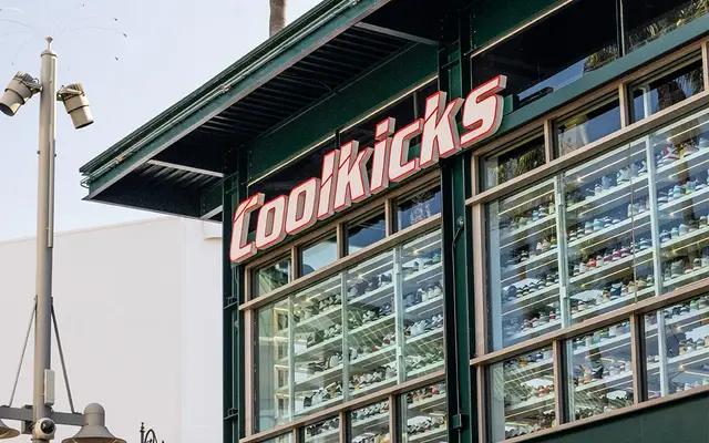 Exterior view of Coolkicks store featuring large windows and a colorful entrance with umbrellas. Palm trees are visible in the background.