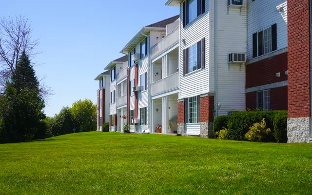 Three-story residential building with red brick and white siding, green lawn in the foreground.