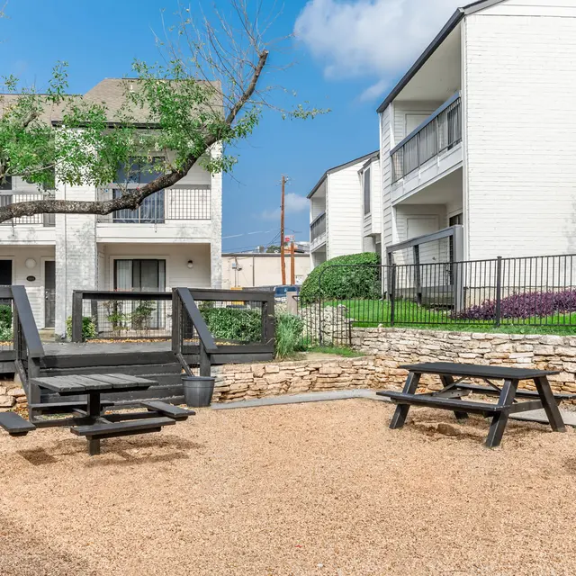 Outdoor picnic area in the courtyard at Aviva at North Plaza, featuring a table, benches, and a grill for residents to enjoy, surrounded by greenery and apartment buildings.