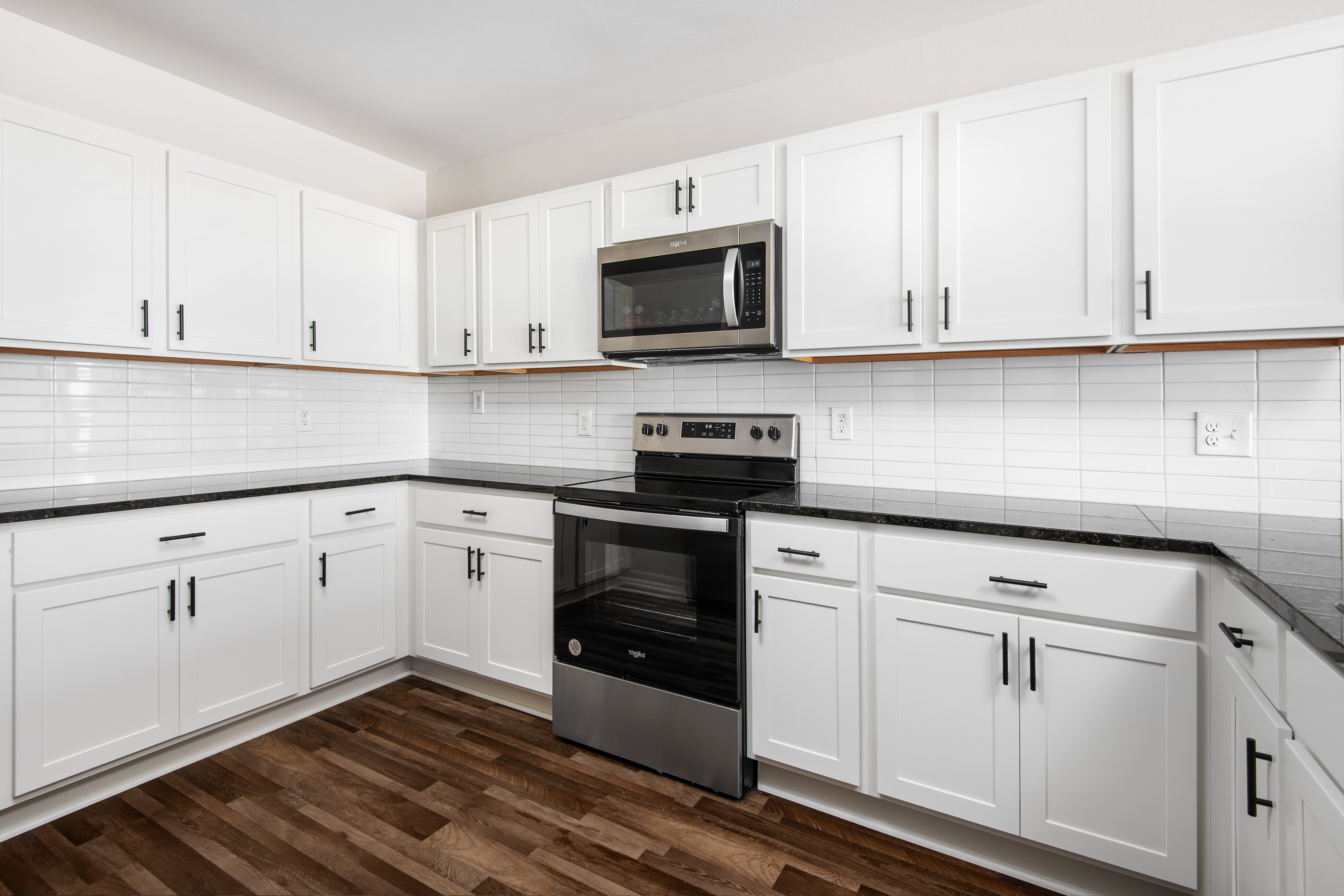 A modern kitchen featuring white cabinetry, a black stove, and wooden flooring.
