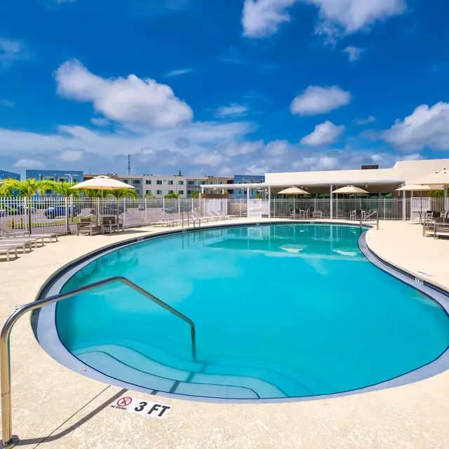 Swimming pool surrounded by lounge chairs, tables with umbrellas, and concrete.