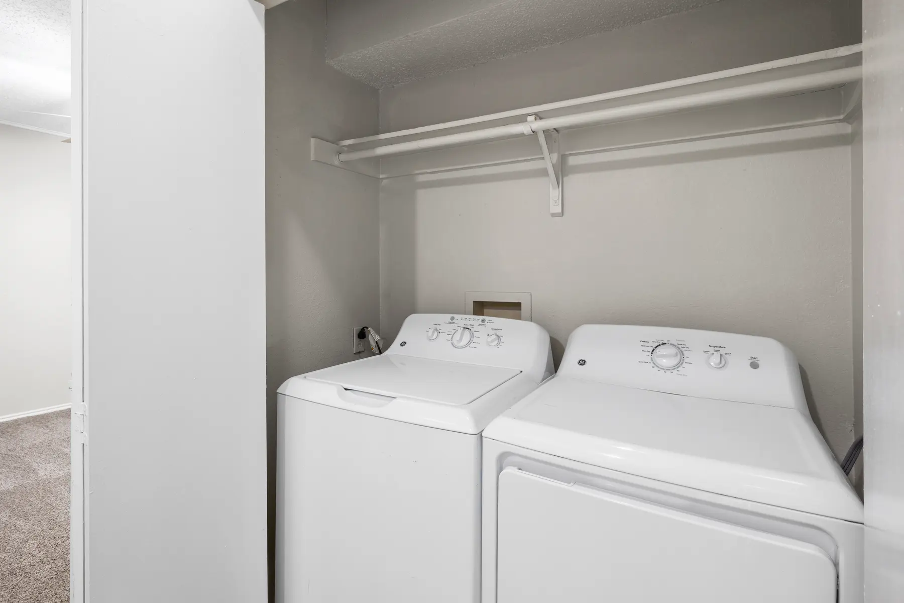 A compact laundry room featuring a white top-loading washing machine and a front-loading dryer side by side against a light gray wall.