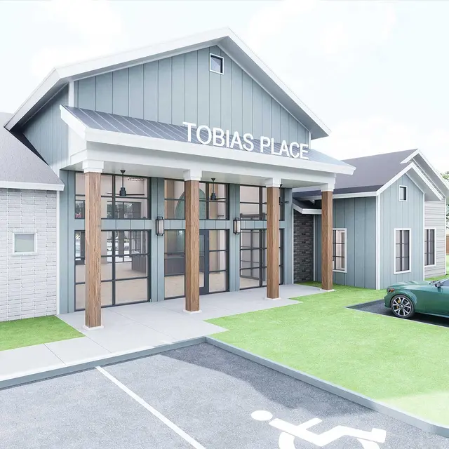 Modern building with a sign reading "Tobias Place," featuring large front windows, wooden accents, and a nearby parking lot.