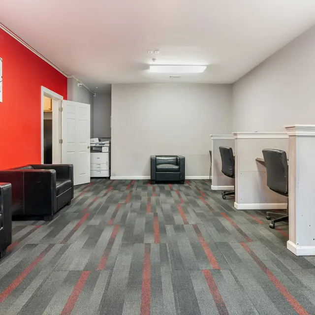 An interior view of an office space featuring black leather chairs, red accent wall, and workstations with chairs.