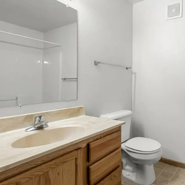 Eagle Ridge A bathroom with a wooden vanity, sink, mirror, toilet, towel bar, and a bathtub with a tiled floor.