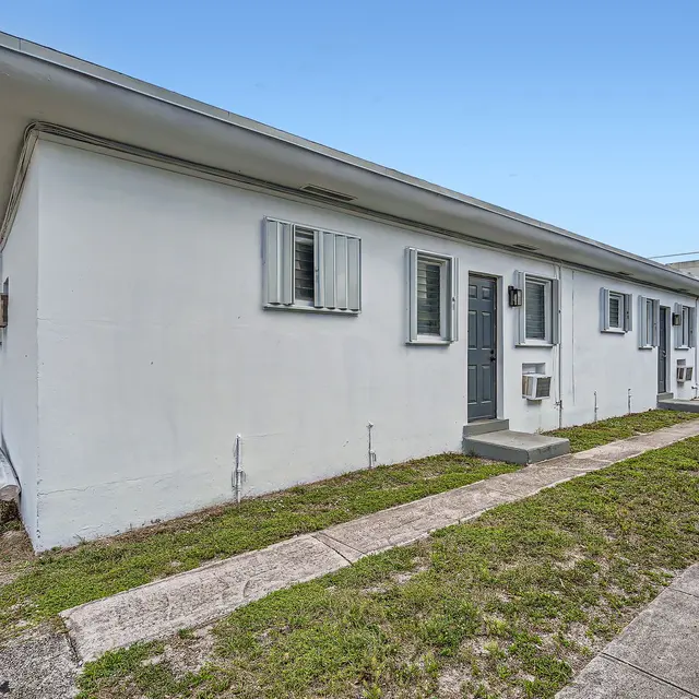 Exterior view of a small apartment complex with white walls and a grassy area in front.