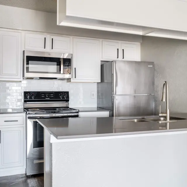 A modern kitchen featuring white cabinets, stainless steel appliances including a microwave and refrigerator, and a dark countertop with a sink.