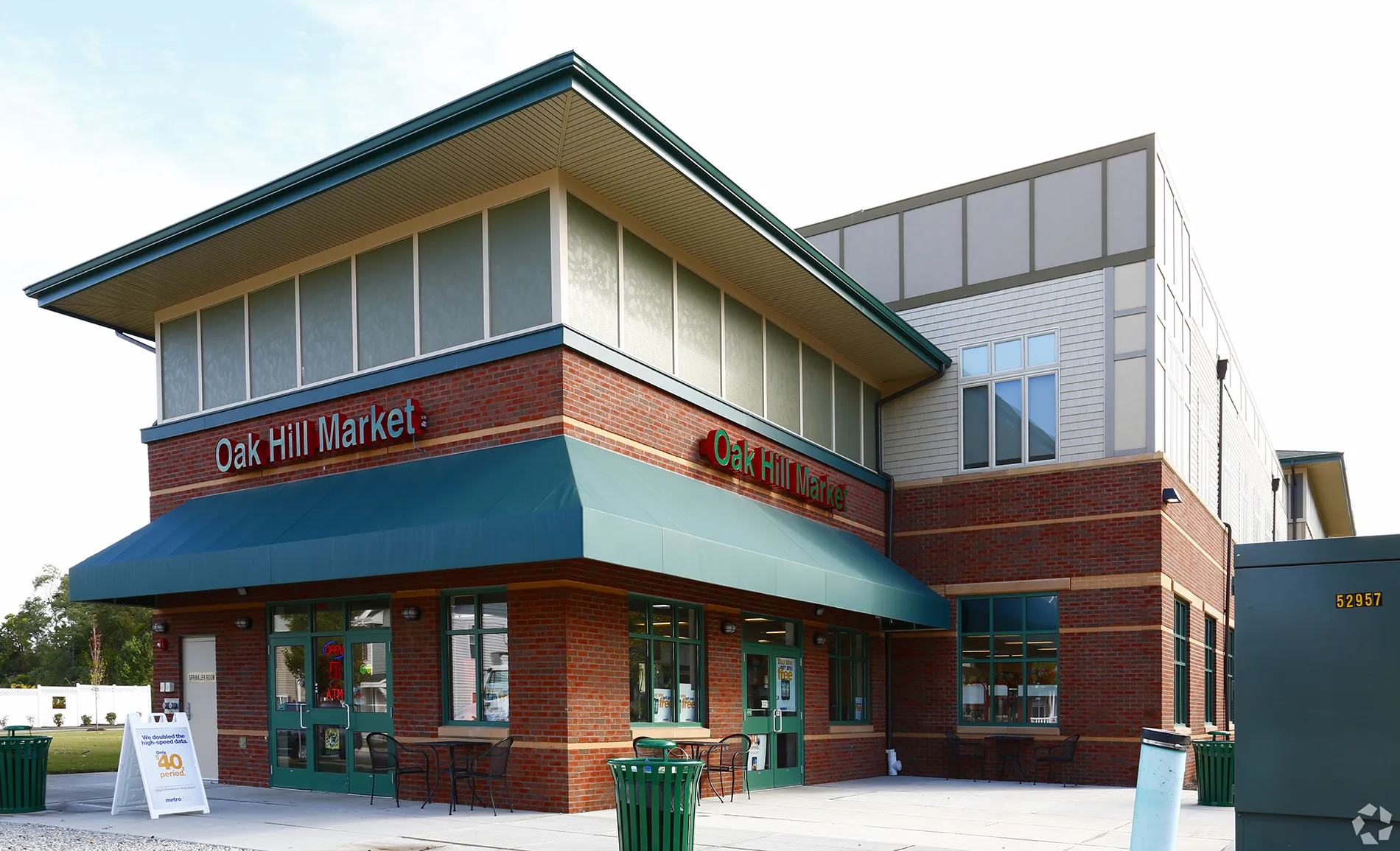 Exterior view of Oak Hill Market, a two-story brick building with large windows and an awning, surrounded by greenery.