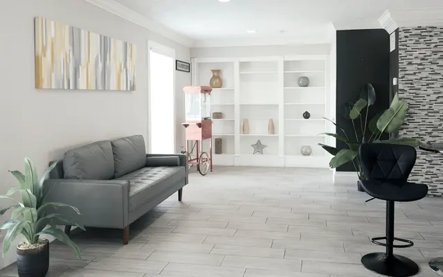 A modern living area featuring a grey sofa, a stylish black chair, and decorative shelves. There's a popcorn machine and plants adding a touch of color and life to the space.