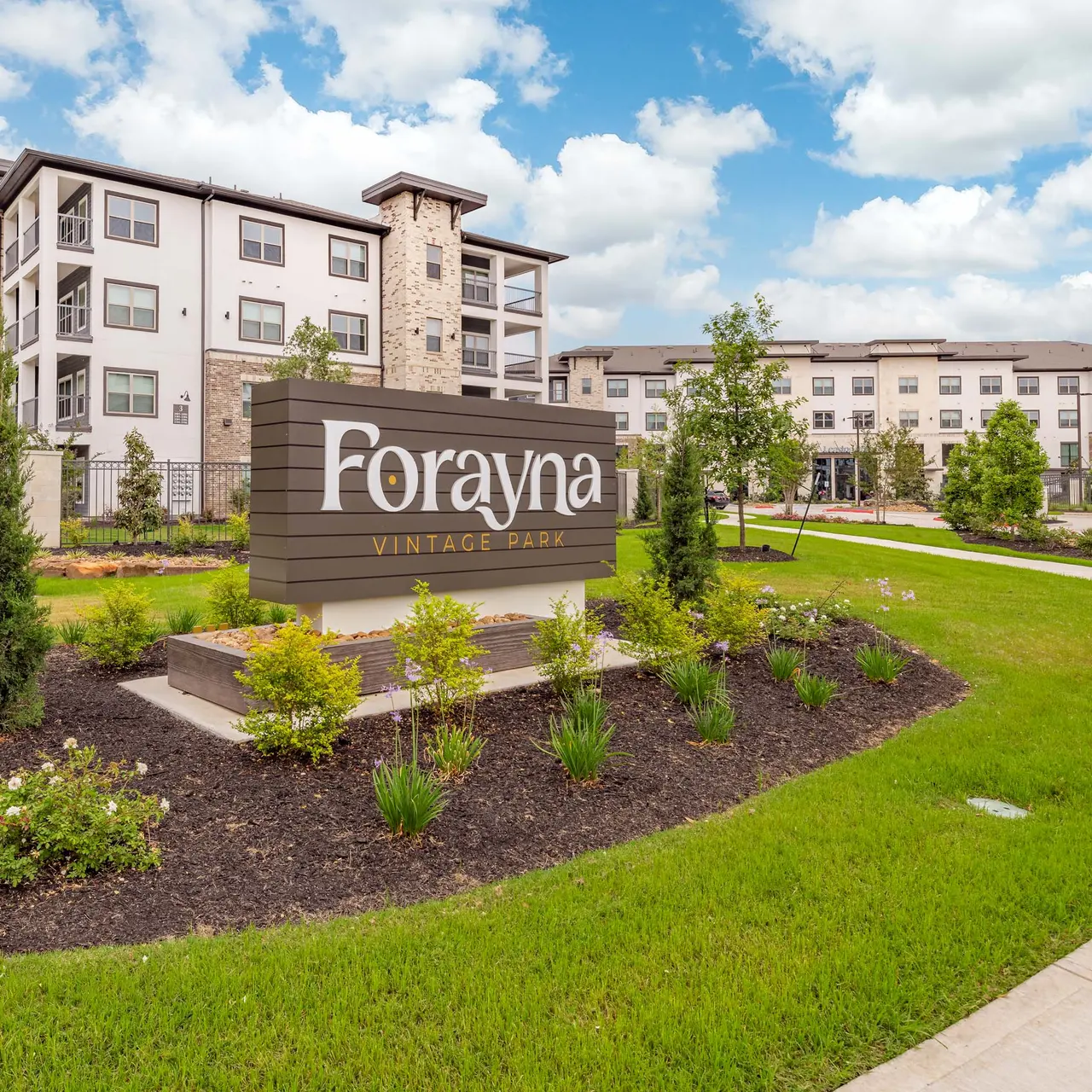 Sign for Forayna Vintage Property with landscaped garden and apartment buildings in the background.