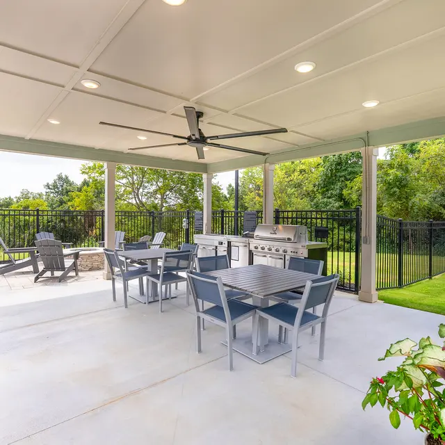 A spacious outdoor patio area featuring a dining set, barbecue grill, and a landscaped view.