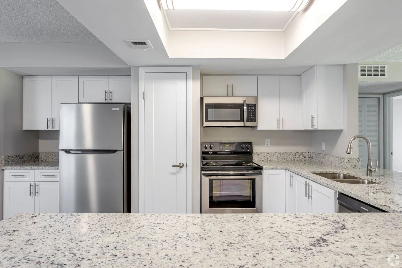 A modern kitchen featuring stainless steel appliances, white cabinetry, and a spacious granite countertop.