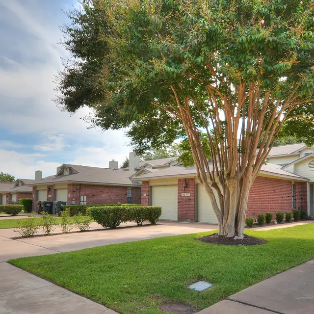 A view of a residential neighborhood with well-maintained lawns, a large tree, and several houses along a paved pathway.