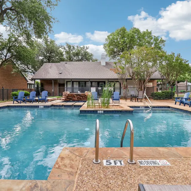 Outdoor swimming pool area with lounge chairs and trees in the background.