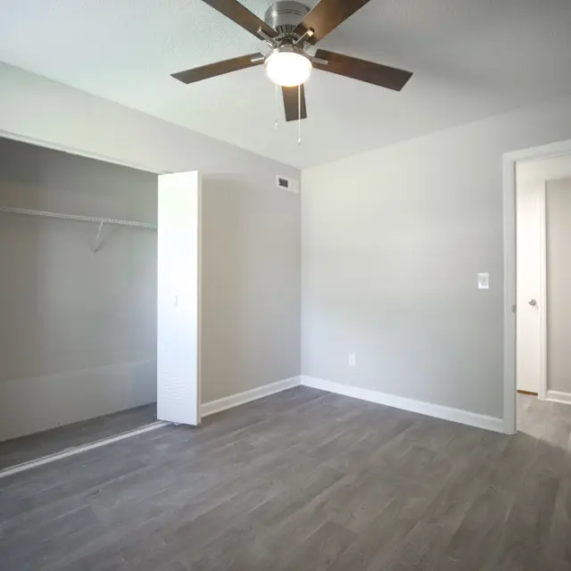A spacious empty bedroom featuring a ceiling fan, light-colored walls, and a closet without doors.
