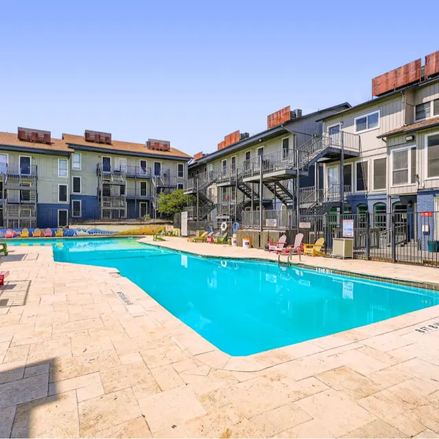 Apartment Complex Pool Area A clear swimming pool surrounded by modern apartment buildings, with colorful lounge chairs and a sunny sky.