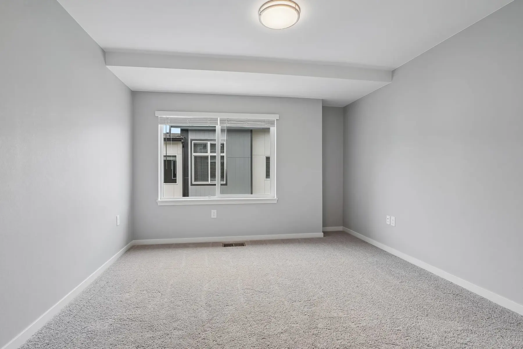 Vacant Bedroom Space A vacant room with light gray walls and carpet, featuring a window that lets in natural light.