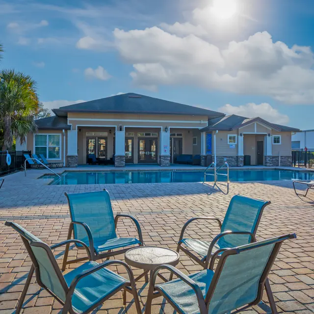 A serene poolside area featuring a swimming pool, lounge chairs, and a clubhouse surrounded by palm trees under a bright sunny sky.